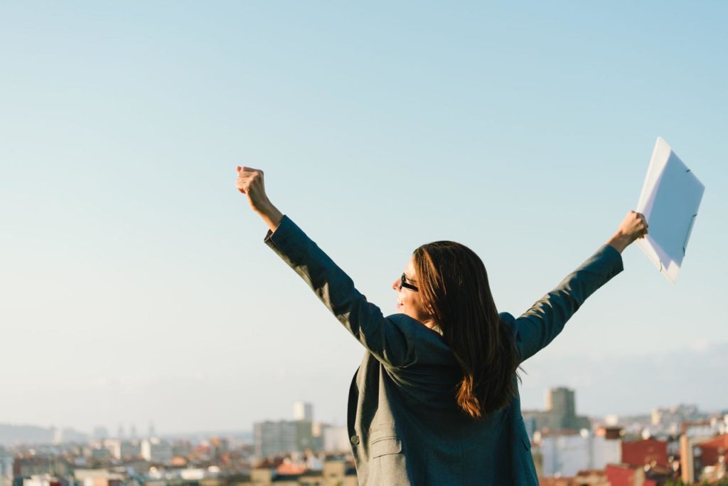 Successful businesswoman with arms up celebrating towards skyline